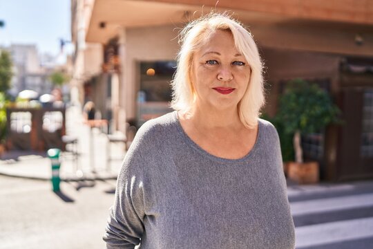 Middle age blonde woman with relaxed expression standing at street