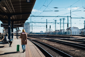 Happy young traveler woman with luggage waiting for train at train station platform