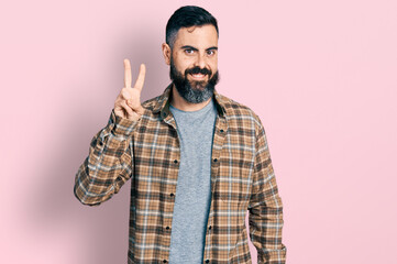 Hispanic man with beard wearing casual shirt showing and pointing up with fingers number two while smiling confident and happy.