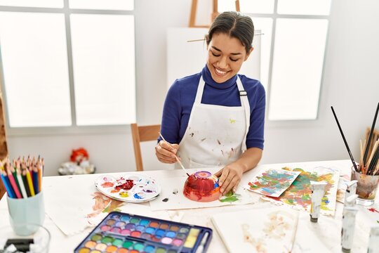 Young latin woman smiling confident painting clay ceramic at art studio