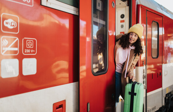 Happy young traveler woman with luggage getting off the train at train station platform
