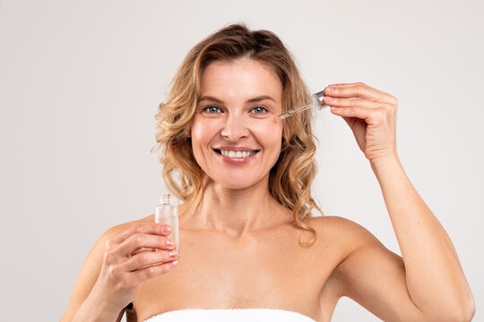 Anti-Age Cosmetics. Attractive Middle Aged Woman Applying Face Serum On Cheek