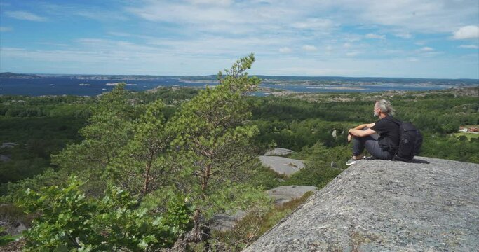 Grey haired man, photographer, sitting on rock, enjoying view
