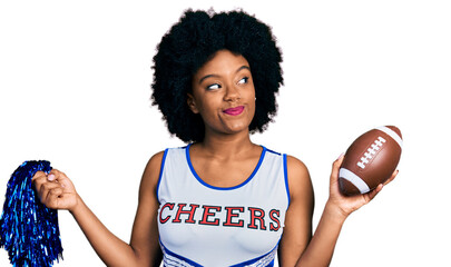 Young african american woman wearing cheerleader uniform holding pompom and football ball smiling...