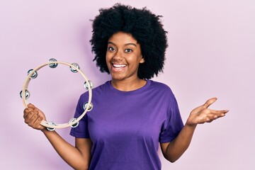 Young african american woman playing tambourine celebrating achievement with happy smile and winner expression with raised hand - Powered by Adobe