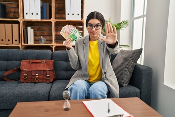 Young hispanic woman working at consultation office holding money with open hand doing stop sign...