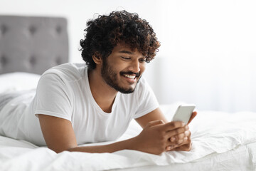 Handsome hindu guy laying on bed with phone, closeup