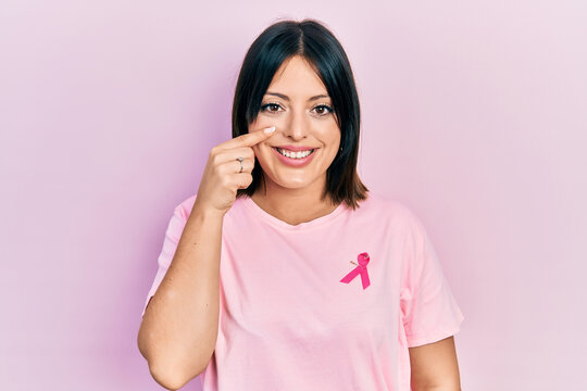Young hispanic woman wearing pink cancer ribbon on t shirt pointing with hand finger to face and nose, smiling cheerful. beauty concept - Powered by Adobe