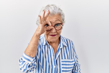 Senior woman with grey hair standing over white background doing ok gesture with hand smiling, eye looking through fingers with happy face.