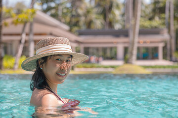 Happy asian woman in red swimsuit and a straw hat relaxing in swimming pool looking at camera by the pool at Koh Mak, Phangnga, Thailand. relax and travel concept. Comfort resort summer vacation