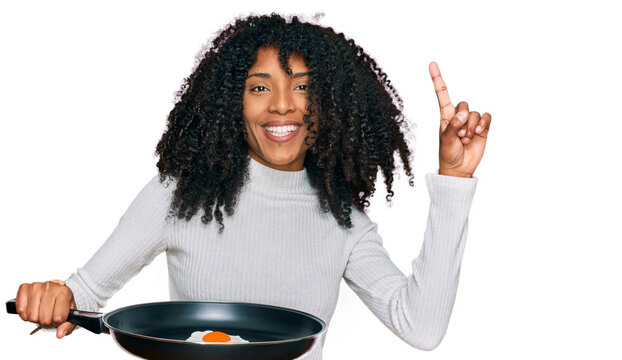 Young african american girl holding skillet with fried egg surprised with an idea or question pointing finger with happy face, number one