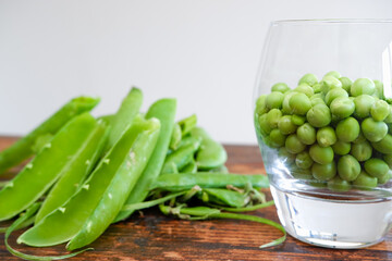 Green peas in glass bowl. fresh pea in the pod with green leaves. green peas on a brown wodden table