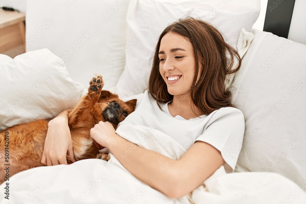 Wall mural young hispanic woman hugging dog lying on bed at bedroom