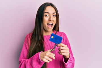 Young hispanic girl cutting credit card using scissors celebrating crazy and amazed for success...