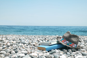 Books and male straw hat on the pebble beach. Concept of reading and relaxing in summer vacation....