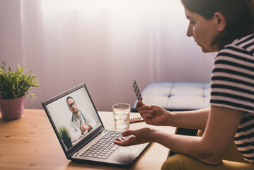 Woman sitting on a sofa and talking with a doctor online using laptop. Telemedicine concept.