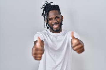 Fototapeta premium African man with dreadlocks wearing casual t shirt over white background approving doing positive gesture with hand, thumbs up smiling and happy for success. winner gesture.