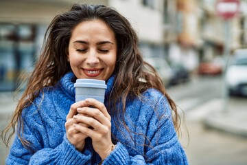 Young hispanic woman smiling happy smelling coffee at the city.