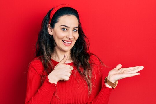 Young hispanic woman wearing casual clothes showing palm hand and doing ok gesture with thumbs up, smiling happy and cheerful