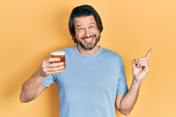 Middle age caucasian man drinking a pint of beer smiling happy pointing with hand and finger to the side