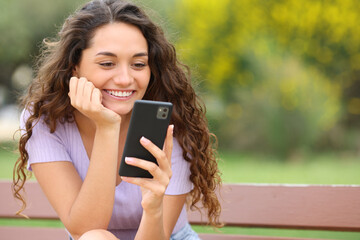 Happy woman using smart phone sitting in a park
