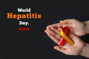 World hepatitis day. Adult hands holding red yellow ribbon on black background. Awareness of prevention and treatment viral hepatitis. Liver cancer. World cancer day. copy space. banner