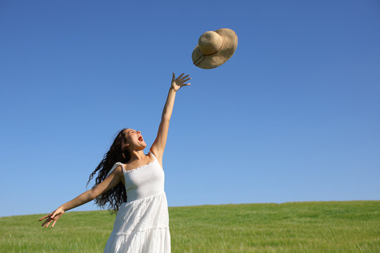 Happy woman throwing pamela hat to the air in a field