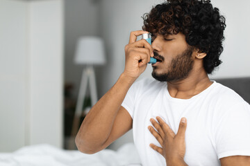 Indian guy suffering from asthma, using inhaler in bed - obrazy, fototapety, plakaty