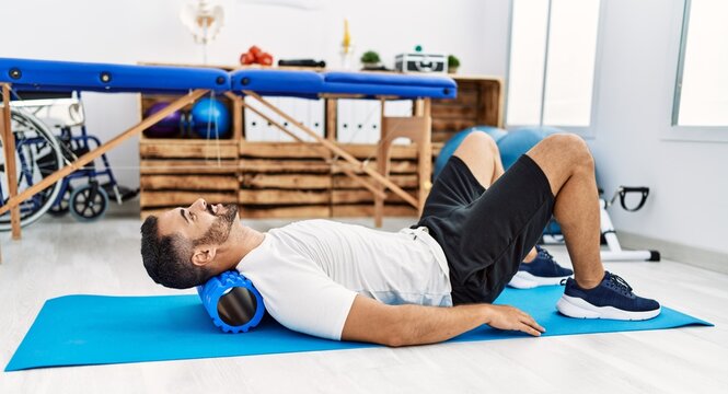 Young hispanic man patient smiling confident having neck rehab session using foam roller at clinic