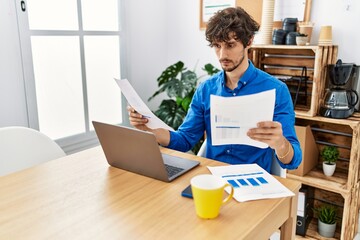 Young hispanic man reading document working at office