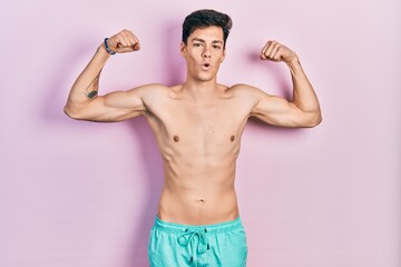 Young hispanic man wearing swimwear shirtless showing arms muscles smiling proud. fitness concept.