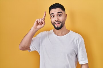 Young handsome man wearing casual t shirt over yellow background pointing finger up with successful idea. exited and happy. number one.