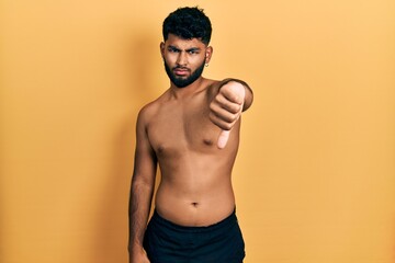 Arab man with beard wearing swimwear shirtless looking unhappy and angry showing rejection and negative with thumbs down gesture. bad expression.