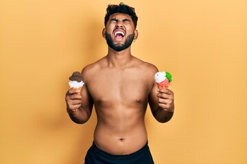Arab man with beard wearing swimwear eating two ice cream cones angry and mad screaming frustrated...