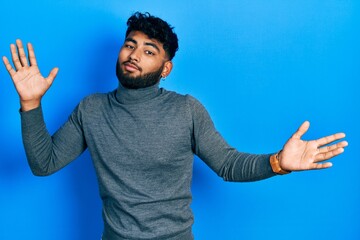 Arab man with beard wearing turtleneck sweater clueless and confused expression with arms and hands...