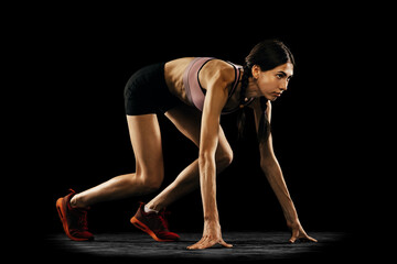 Fototapeta na wymiar Ready to start. Studio shot of young muscular woman running isolated on black background. Sport, track-and-field athletics, competition and active lifestyle concept