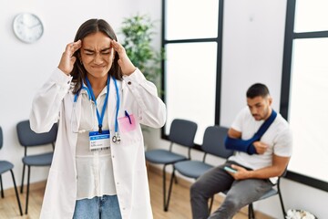 Fototapeta premium Young asian doctor woman at waiting room with a man with a broken arm with hand on head for pain in head because stress. suffering migraine.