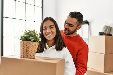 Young latin couple smiling happy holding cardboard box at new home.