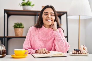 Obraz na płótnie Canvas Young hispanic woman reading book having breakfast at home