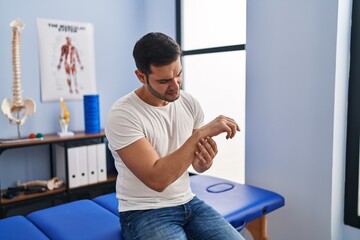 Young hispanic man injured physiotherapy patient suffering for wrist pain at rehab clinic