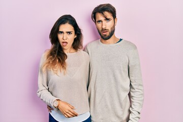 Young hispanic couple wearing casual clothes in shock face, looking skeptical and sarcastic, surprised with open mouth