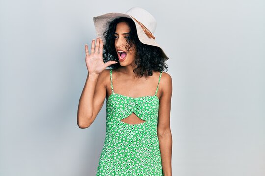 Young latin girl wearing summer hat shouting and screaming loud to side with hand on mouth. communication concept.