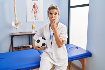 Young woman working at football therapy clinic covering mouth with hand, shocked and afraid for mistake. surprised expression - Powered by Adobe