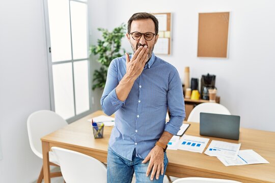 Middle age hispanic man with beard wearing business clothes at the office bored yawning tired covering mouth with hand. restless and sleepiness.