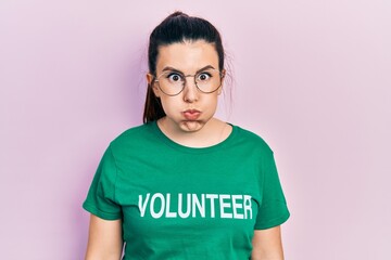 Young hispanic woman wearing volunteer t shirt puffing cheeks with funny face. mouth inflated with...