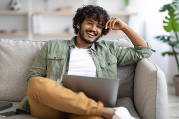 Happy indian guy using notebook at home
