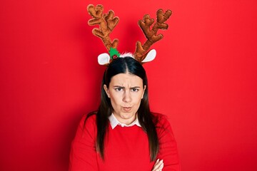 Young hispanic woman wearing cute christmas reindeer horns skeptic and nervous, disapproving...