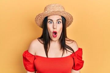 Young hispanic woman wearing summer hat afraid and shocked with surprise expression, fear and excited face.