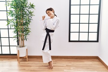 Young hispanic girl wearing karate kimono and black belt very happy and excited doing winner gesture with arms raised, smiling and screaming for success. celebration concept.