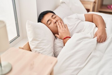 Fototapeta na wymiar Young chinese man lying on bed yawning at bedroom